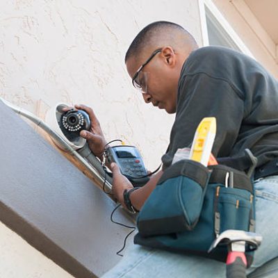 A technician uses a monitor to adjust a security camera while installing the system to the exterior of a building.